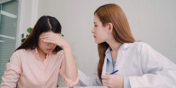 Doctor talking to unhappy teenage patient in exam room. Asian woman doctor encouragement and support to cancer patient after consult and examine health in medical clinic or hospital.